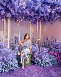 a woman sitting on a swing surrounded by purple flowers