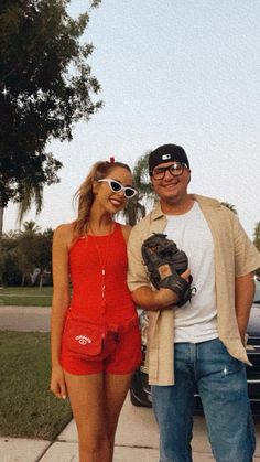 a man standing next to a woman in front of a car on a sidewalk wearing sunglasses and holding a catchers mitt