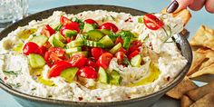 a bowl filled with cucumber and tomatoes on top of a table next to chips