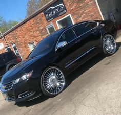 a black car parked in front of a brick building with chrome wheels and rims