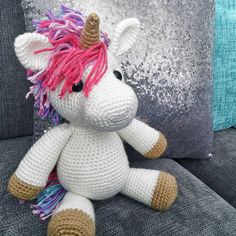 a crocheted stuffed unicorn sits on a couch