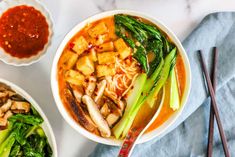 two bowls filled with food next to chopsticks and sauce on a white table