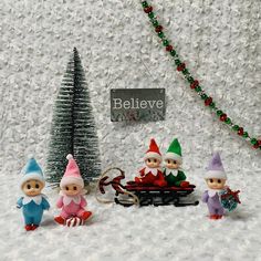 three elf figurines sitting in front of a christmas tree with a sleigh