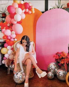 a woman is sitting on a chair in front of some balloons and flowers with her legs crossed