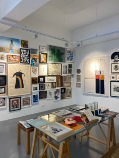 an art gallery with multiple pieces of artwork on the wall and wooden tables in front of them