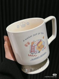 a woman holding a coffee mug with an image of a bus on it and the words,'awarm cup of tea rabbit series '