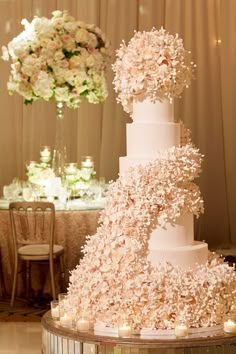 a wedding cake with white flowers on top and candles around the bottom, in front of a chandelier