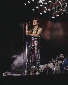 a man standing on top of a stage with a microphone in his hand and wearing sequin pants