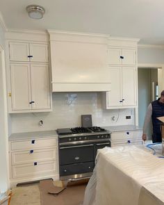 two men working in a kitchen with white cabinets and an electric stove top oven under construction