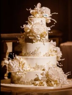 a three tiered wedding cake with white flowers on the bottom and gold trimmings