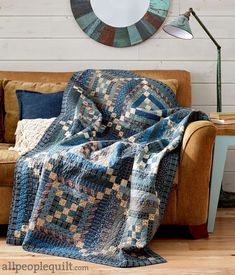 a couch with a quilt on it in front of a round mirror and wall clock