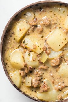 a bowl filled with meat and potatoes on top of a white countertop next to a spoon