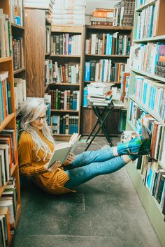 a woman sitting on the floor reading a book in front of a bookshelf