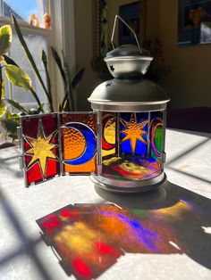 a lit candle sitting on top of a table next to stained glass pieces with sun and moon designs