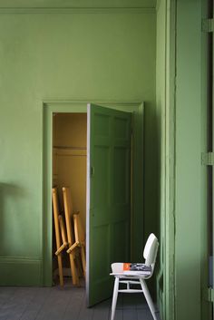 a green room with a white chair in the corner and an open door leading to another room