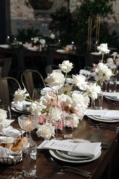 the table is set with white and pink flowers in vases, silverware, and napkins