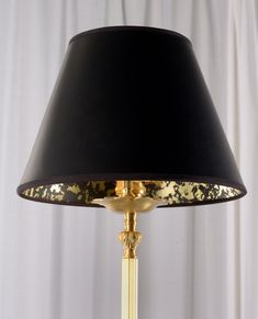 a lamp with a black shade on it and gold trimming around the bottom part