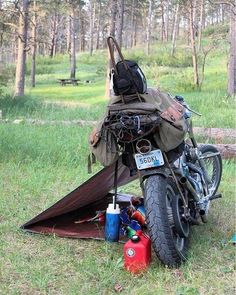 a motorcycle parked next to a tent in the grass with camping gear on it's back