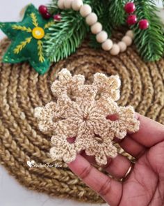 a hand holding a crocheted snowflake ornament in front of a wreath