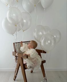 a baby sitting in a chair with white balloons