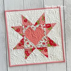 a quilted wall hanging with a heart in the center on a white wooden surface