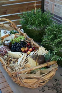 a wicker basket filled with assorted cheeses and fruit on a table outside