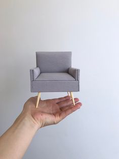 a hand holding a miniature chair in front of a white wall