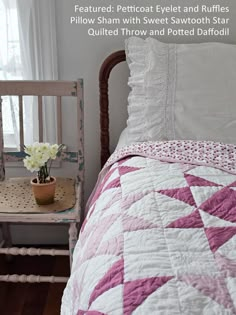 a pink and white quilt on a bed next to a chair with flowers in it