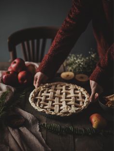 a person cutting into a pie on top of a wooden table with apples and other fruit