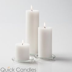 three white candles sitting next to each other on top of a glass table with one candle lit