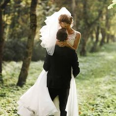 the bride and groom are walking through the woods on their wedding day, carrying each other