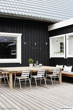 a wooden table sitting on top of a wooden floor next to a black building with white windows