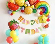 a birthday party with balloons, fruit and streamers hanging on the wall in front of it