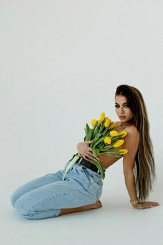 a beautiful young woman laying on the ground with yellow tulips in her hands