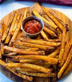 french fries with ketchup on a wooden platter next to a bowl of sauce