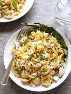 a white plate topped with pasta covered in cheese and vegetables next to a fork on top of a table