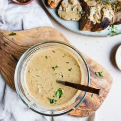 a glass bowl filled with soup next to some grilled meat on a cutting board