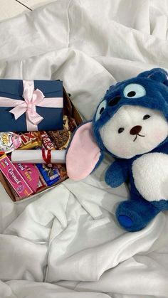 a stuffed animal sitting next to a box of candy on a white bed with sheets