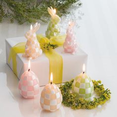 three candles are sitting next to some wrapped presents with bows and greenery on them