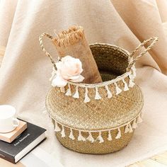 a woven basket with tassels and a flower on it next to a book