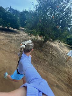 a woman riding a bike down a dirt road next to a forest filled with trees