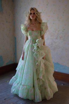 This is a gown fit for a rather *provocative* queen, featuring a liberally drawn ruffled leg slit, and layers and layers of voluminous skirt. Against an acid green backdrop, vivid blush and pearl blooms burst forth in a mesmerizing, hallucinogenic floral display, while the shoulder ruffles at the sleeve and underwire cups highlight the bust. The devastatingly dramatic bustling skirt—which can be worn bustled up for a bouffant effect or down for a seriously glamorous train—is the standout feature Silk Dressing Gown, Corset Skirt, Puff Dress, Knitted Coat, Floral Display, Bridal Gown, In Bloom, Fancy Dresses, Pretty Dresses