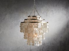 a chandelier hanging from a chain in front of a gray wall with light coming through it