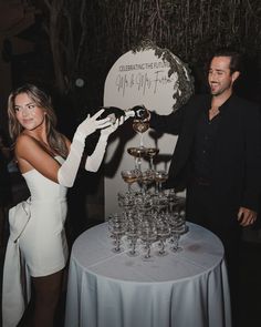 a man standing next to a woman in front of a table filled with wine glasses