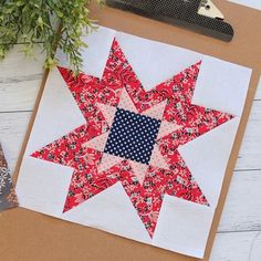 a red and white quilted star on top of a piece of paper next to a potted plant