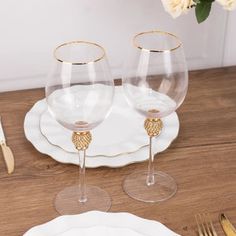 two wine glasses sitting on top of a wooden table next to silverware and flowers