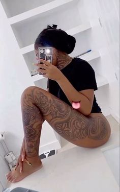 a woman with tattoos taking a selfie in her bathroom while sitting on the toilet