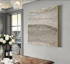 a dining room table with wine glasses and flowers on it in front of a large painting