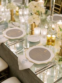 the table is set with white flowers and gold place settings, candles and napkins