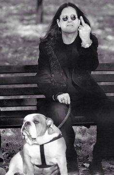 a woman sitting on a bench next to a dog and giving the peace sign with her hand